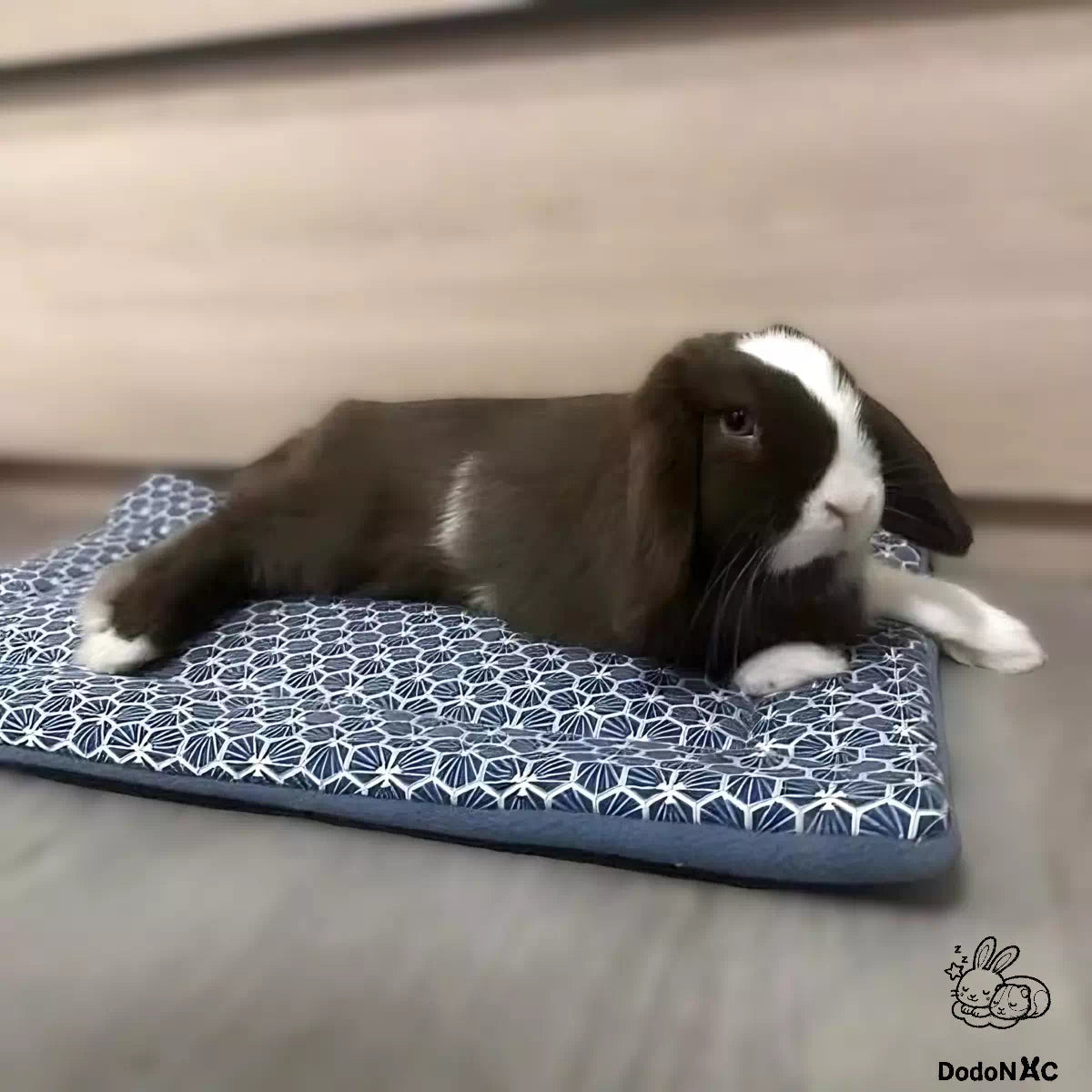 Lapin allongé sur son tapis moelleux douillé et confortable dodoNAC personnalisé avec un tissu motif géométrique et une polaire bleue