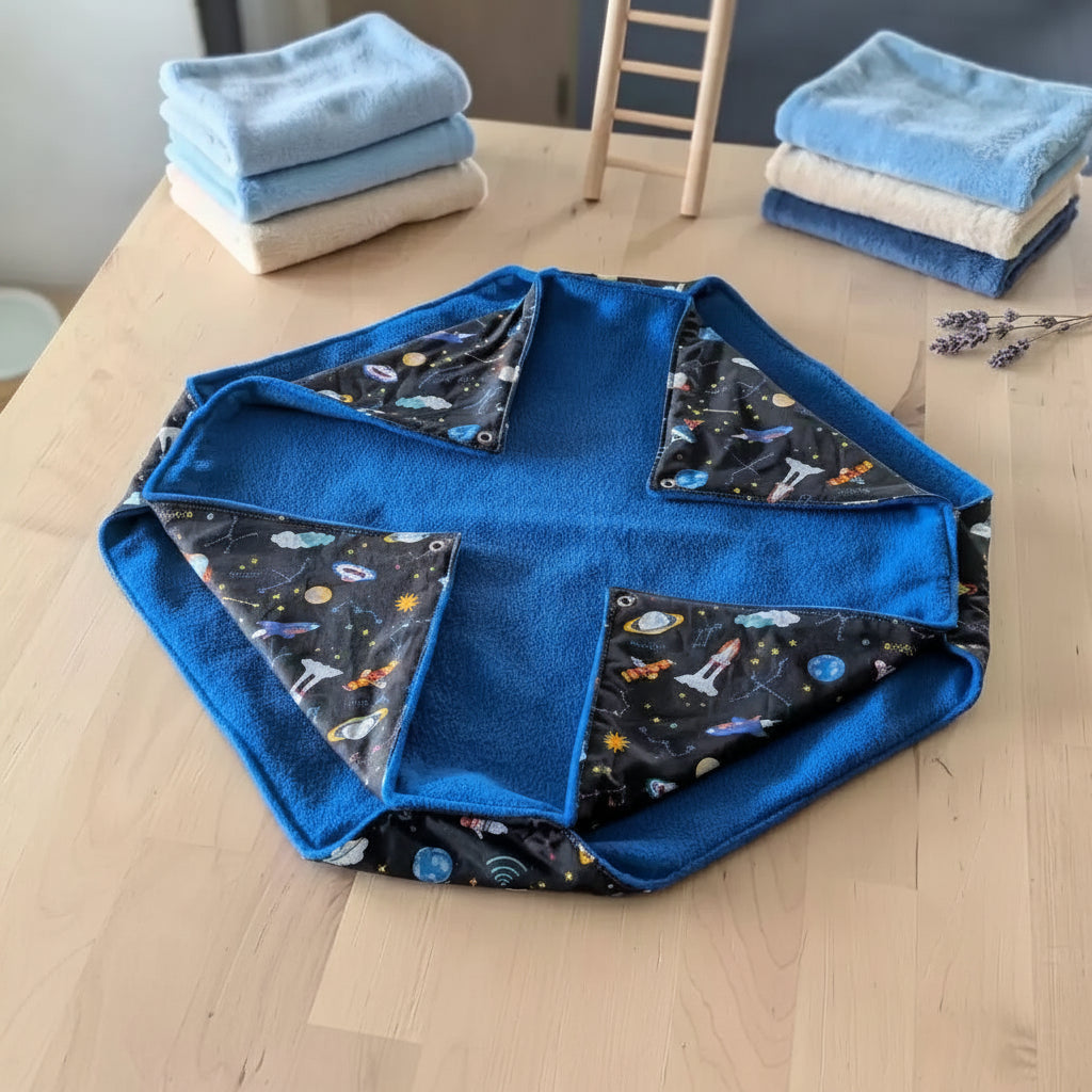 Grand hamac double de taille L pour furets et rats posé sur une table en bois clair. Le dodo suspendu possède un tissu noir imprimé de fusées et de planètes, et un intérieur en polaire bleu roi ultra doux.