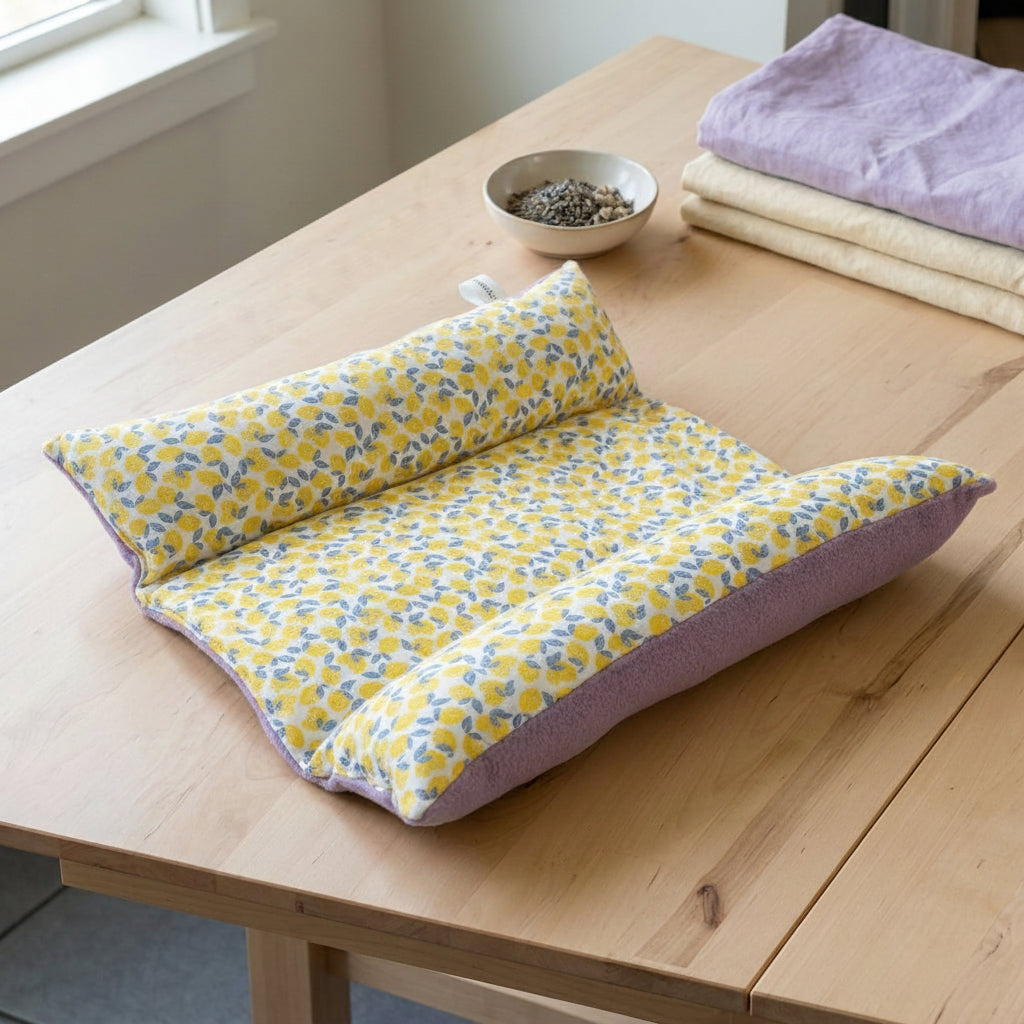 Lit ergonomique Snugabun Solo pour un lapin, avec tissu imprimé mini-citrons jaunes et envers en polaire mauve, posé sur une table en bois clair.
