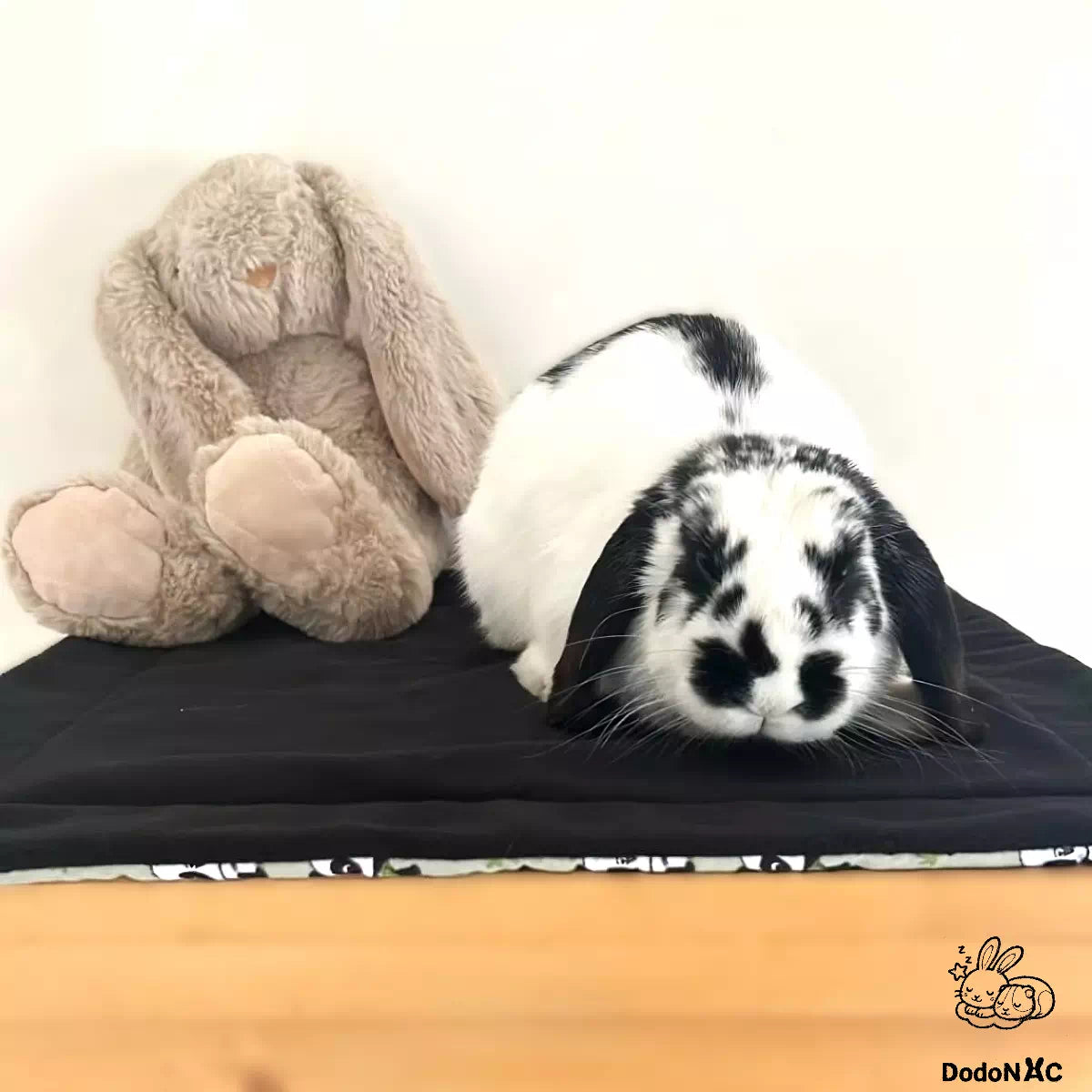 Photo client d'un lapin avec sa peluche allongé sur son tapis litiére absorbant dodoNAC personnalisé avec un tissu motif panda et polaire noire 