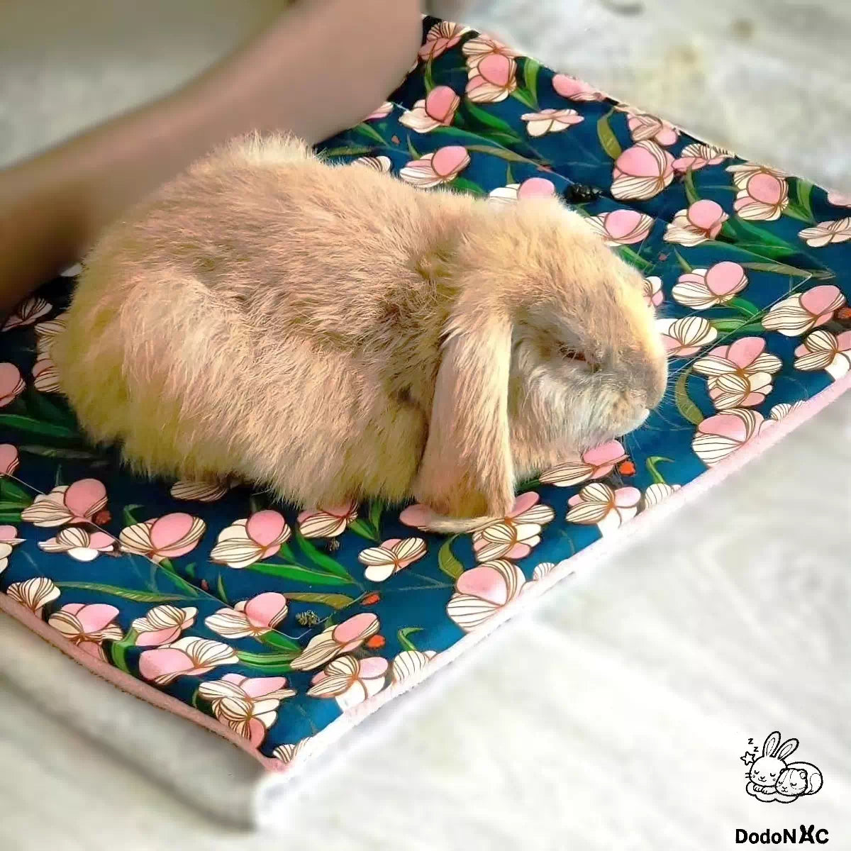 Photo client d'un lapin allongé sur son tapis litiére absorbant dodoNAC taille L personnalisé avec un tissu motif floral et polaire rose poudré